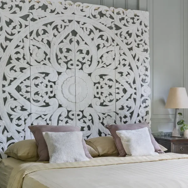 A carved white wooden headboard with an intricate floral and scroll design.